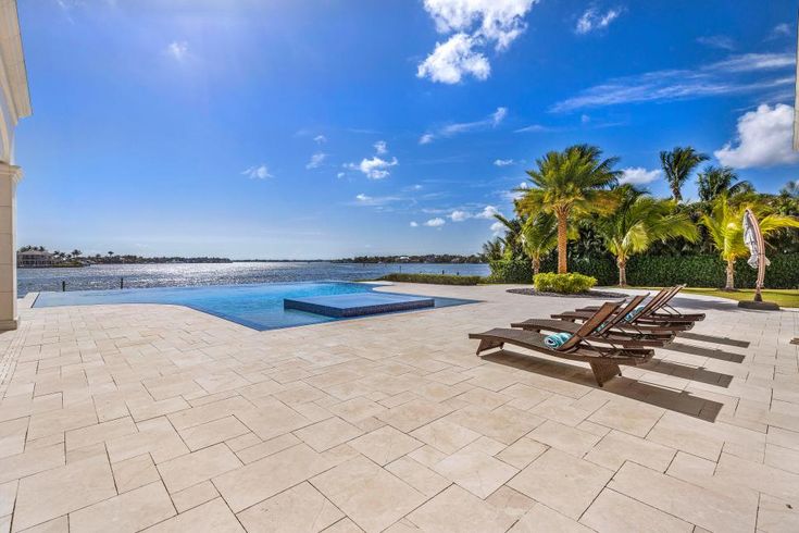 an empty swimming pool with lounge chairs and palm trees in the foreground, on a sunny day