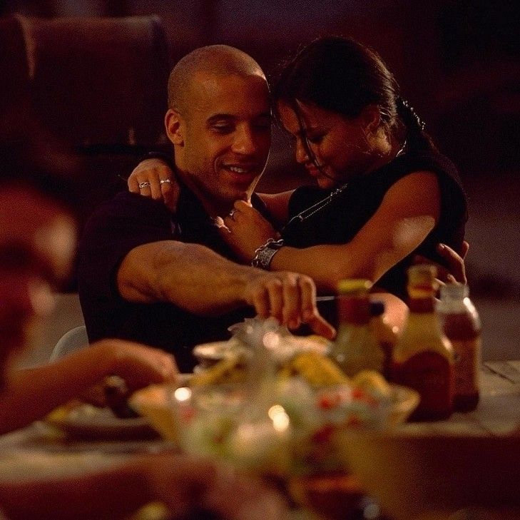 a man and woman hugging each other at a dinner table with food on the plate