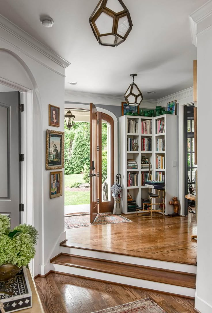 an entry way with bookshelves and wooden floors in the middle, surrounded by greenery