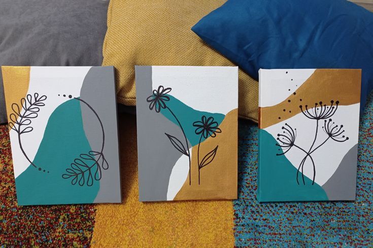 three paintings are sitting on the floor next to a pillow and throw pillow, one is blue