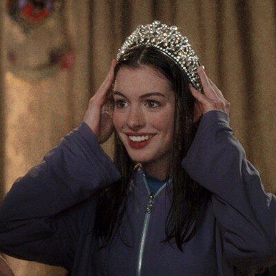 a woman wearing a tiara and smiling at the camera while holding her hair in front of her head