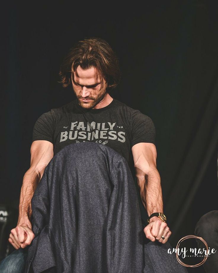 a man with long hair is sitting on a chair and has his hands in his pants