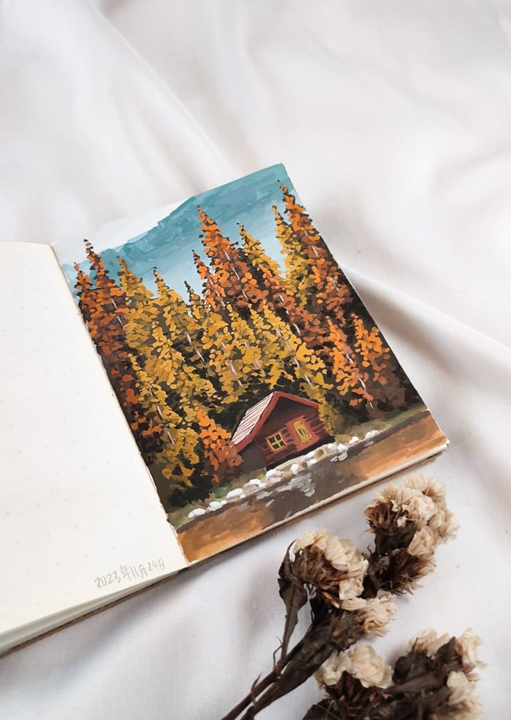 an open book sitting on top of a bed next to dried flowers and cotton buds