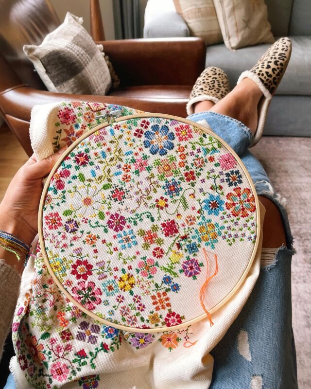 a woman sitting on a couch holding a cross - stitched floral design