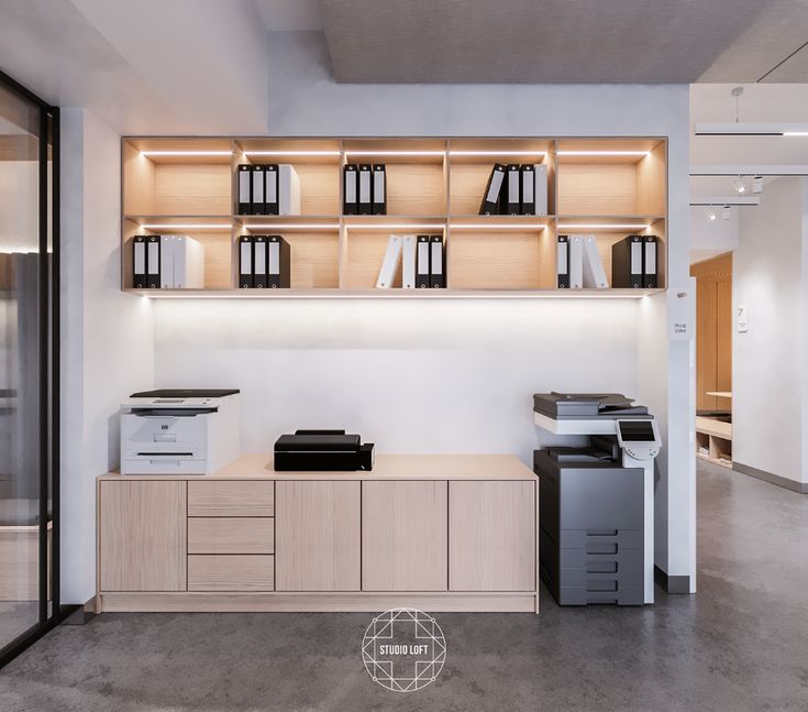 an office with white walls and wooden shelves filled with black and white items, including printer equipment