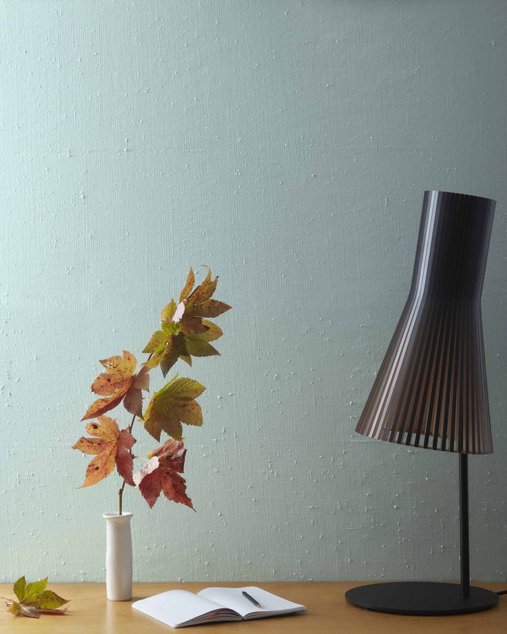 a table with a book and a lamp on it next to a vase filled with leaves