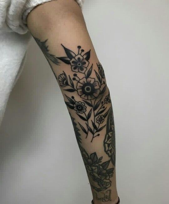 a woman's arm with flowers and leaves on her left forearm, in black ink