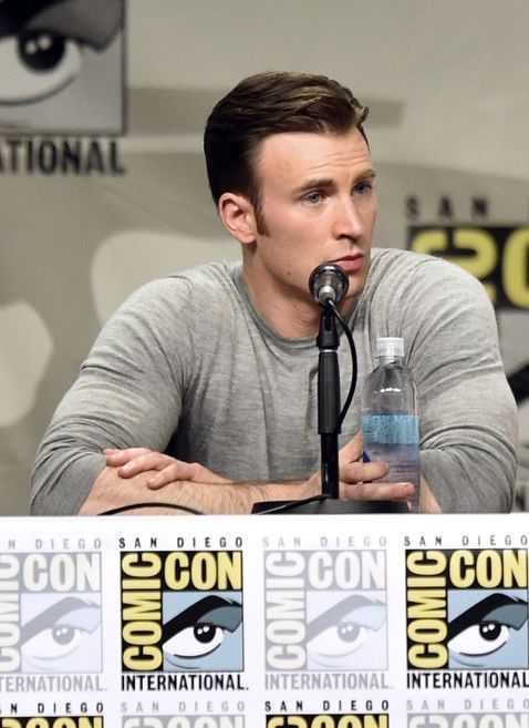 a man sitting at a table with a microphone in front of him and an eyeball on the wall behind him