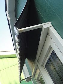 an umbrella is hanging from the side of a green house with white trim on it