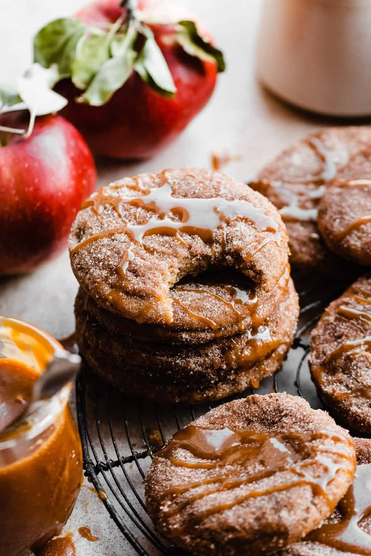 apples and cinnamon donuts on a cooling rack with caramel sauce in the background