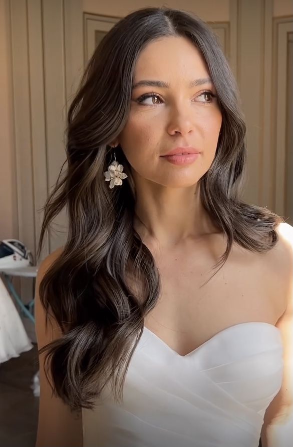 a woman in a strapless white dress with long dark hair and flower clip earrings