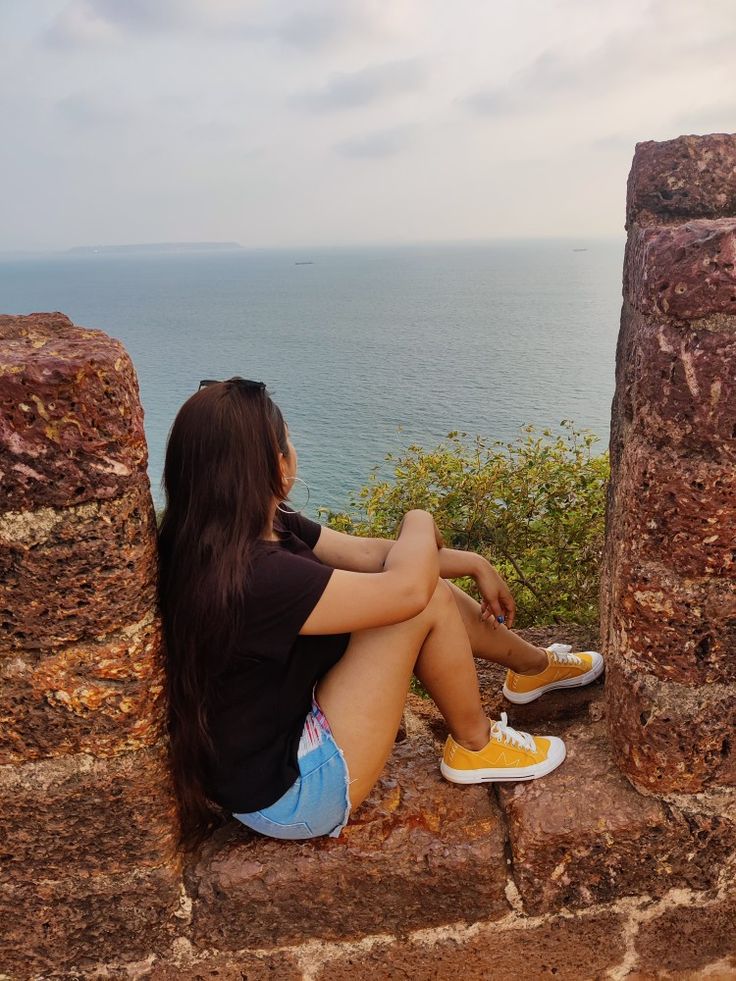 a woman sitting on top of a stone wall next to the ocean