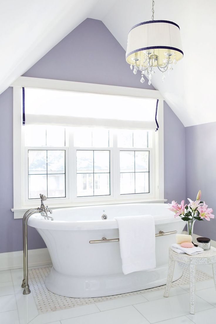 a white bath tub sitting under a window next to a table with flowers on it