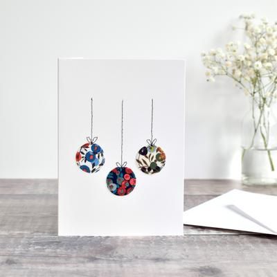 a card with two earrings hanging from it's side on a table next to a vase