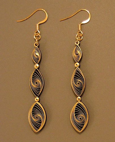 two long gold and black earrings on a brown surface with one dangling from the ear