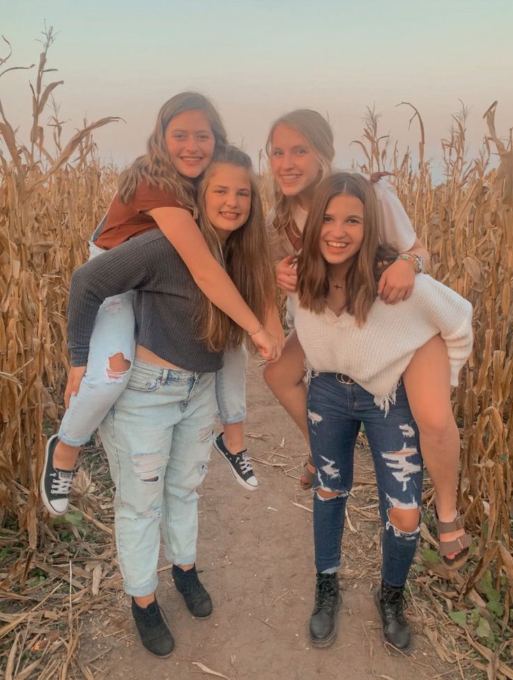 four girls are posing for the camera in front of a corn field with their arms around each other