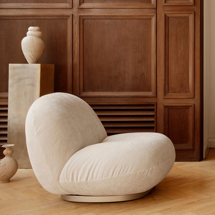 a white chair sitting on top of a hard wood floor next to a tall vase