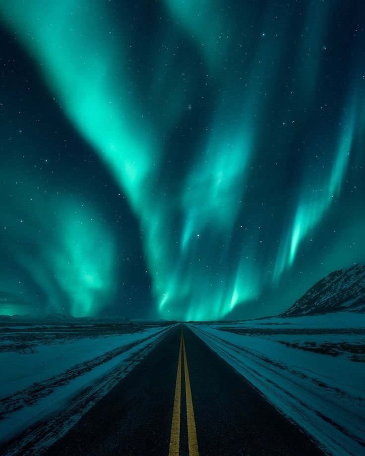 an empty road with the aurora lights in the sky