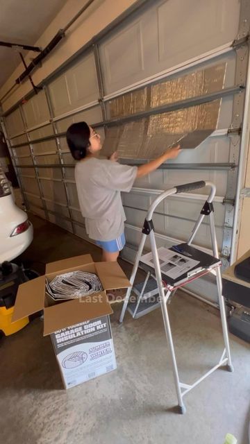 a woman standing in front of a garage door holding onto the side of a ladder