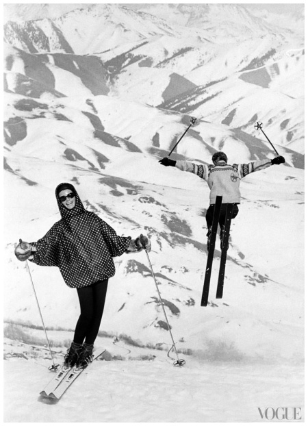 two people on skis in the snow with their arms up and one person wearing goggles