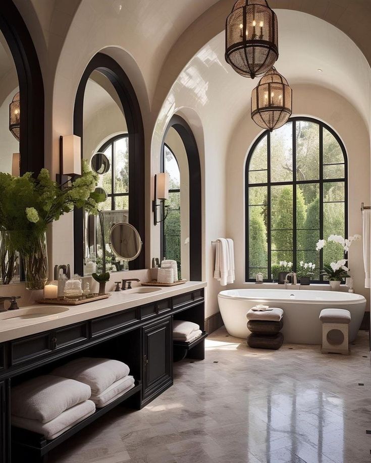 a large bathroom with two sinks and an oval mirror above the tub is surrounded by arched windows