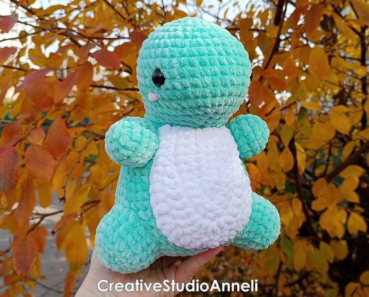 a small crocheted stuffed animal sitting in front of a tree with autumn leaves