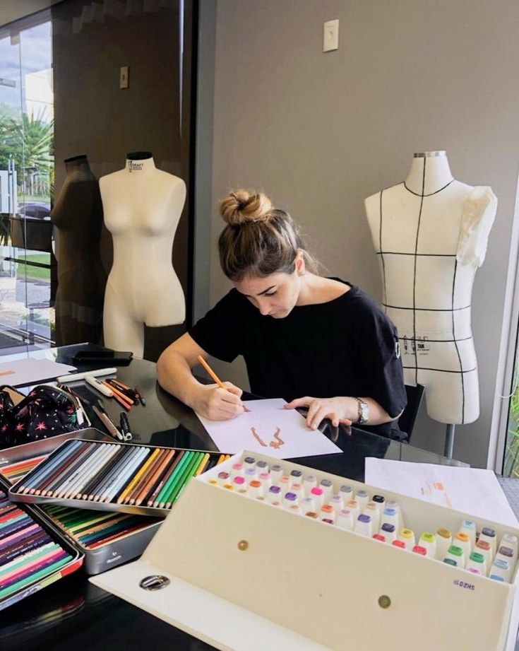 a woman sitting at a table with lots of art supplies in front of her and writing on a piece of paper