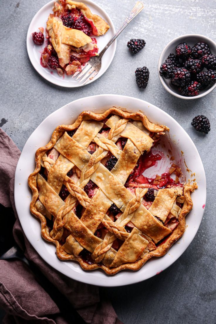 a pie on a white plate with berries in the bowl and other dishes around it