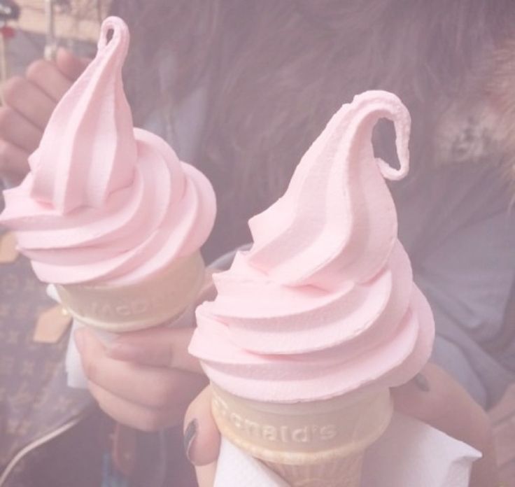 two ice cream cones with pink icing on top are being held by someone's hands