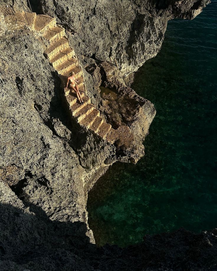 stairs leading down to the ocean from a rocky cliff side area with clear blue water