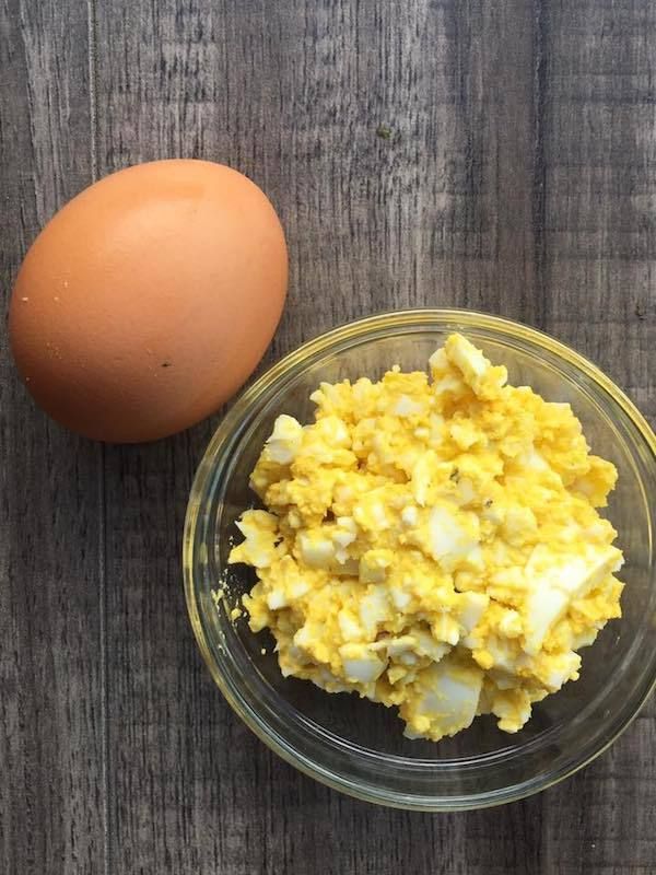 an egg and scrambled eggs in a glass bowl on a wooden table next to each other