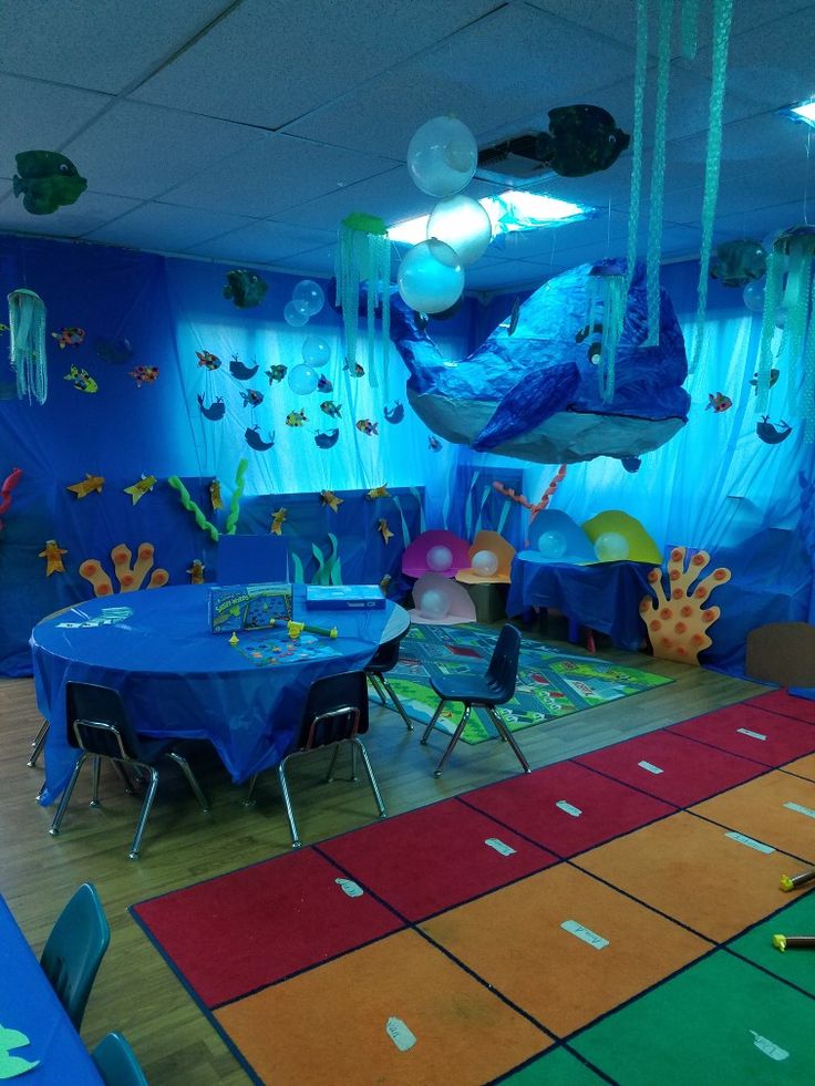 a room decorated in blue and green with fish decorations on the walls, tables and chairs