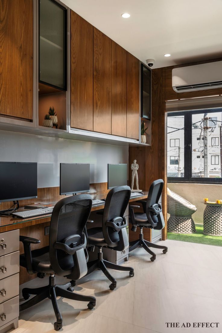 an office with three computer desks and two chairs in front of a large window