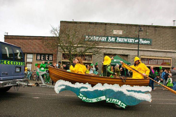 two people in yellow raincoats are riding on a boat down the street while others watch