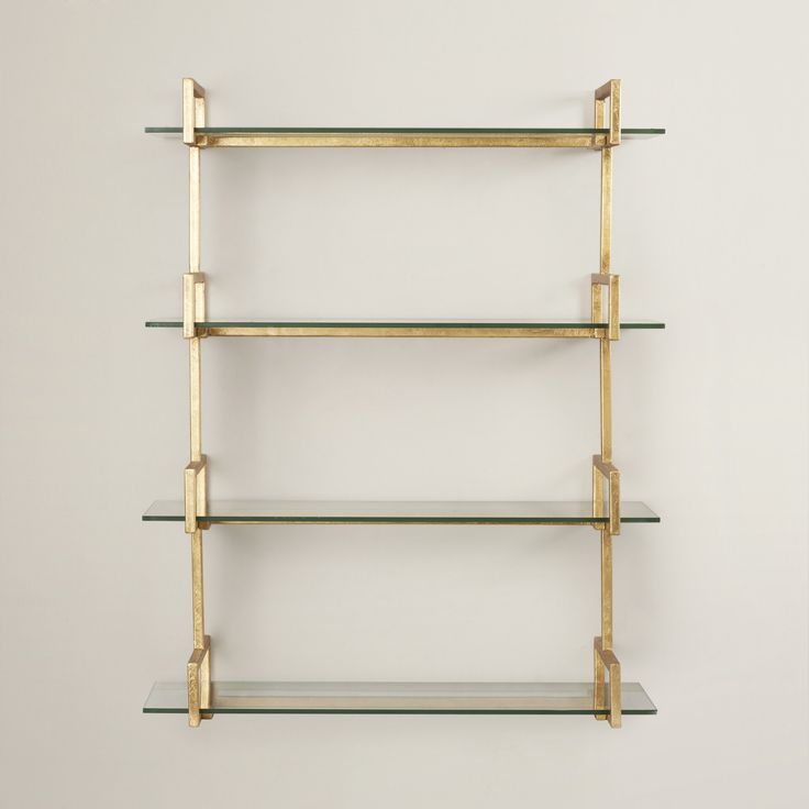 a shelf with glass shelves on each side and gold brackets at the top, against a white wall