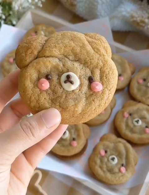 a hand holding up a cookie that has been decorated with teddy bear's eyes