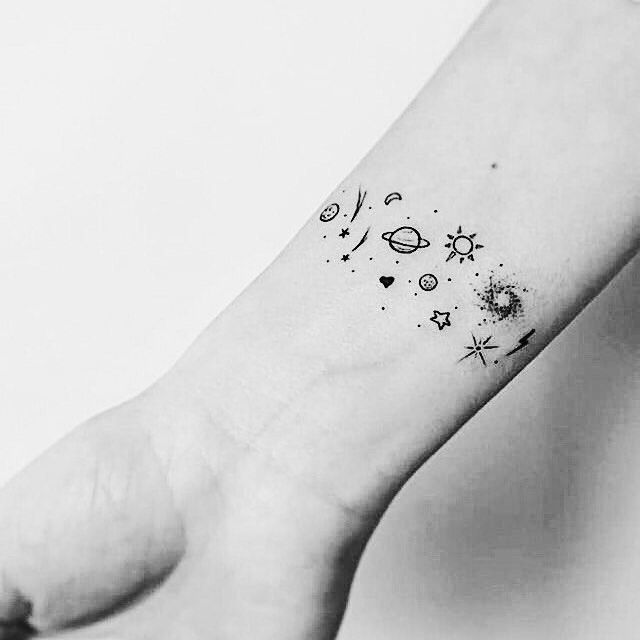 a black and white photo of a small wrist tattoo with stars, planets, and hearts