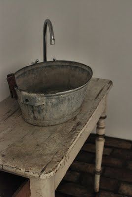 an old wooden table with a large metal bowl on it's top, next to a sink