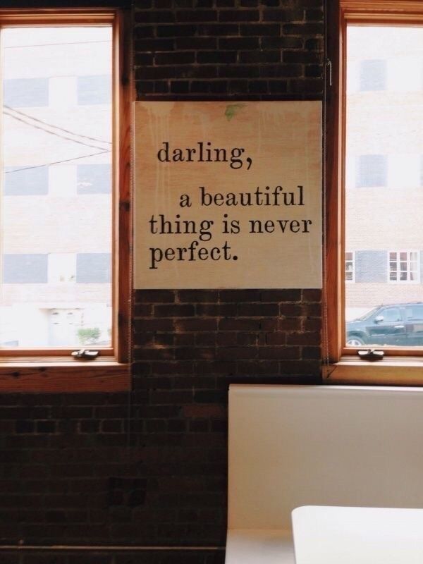 there is a sign on the wall in front of two windows that say, daring a beautiful thing is never perfect