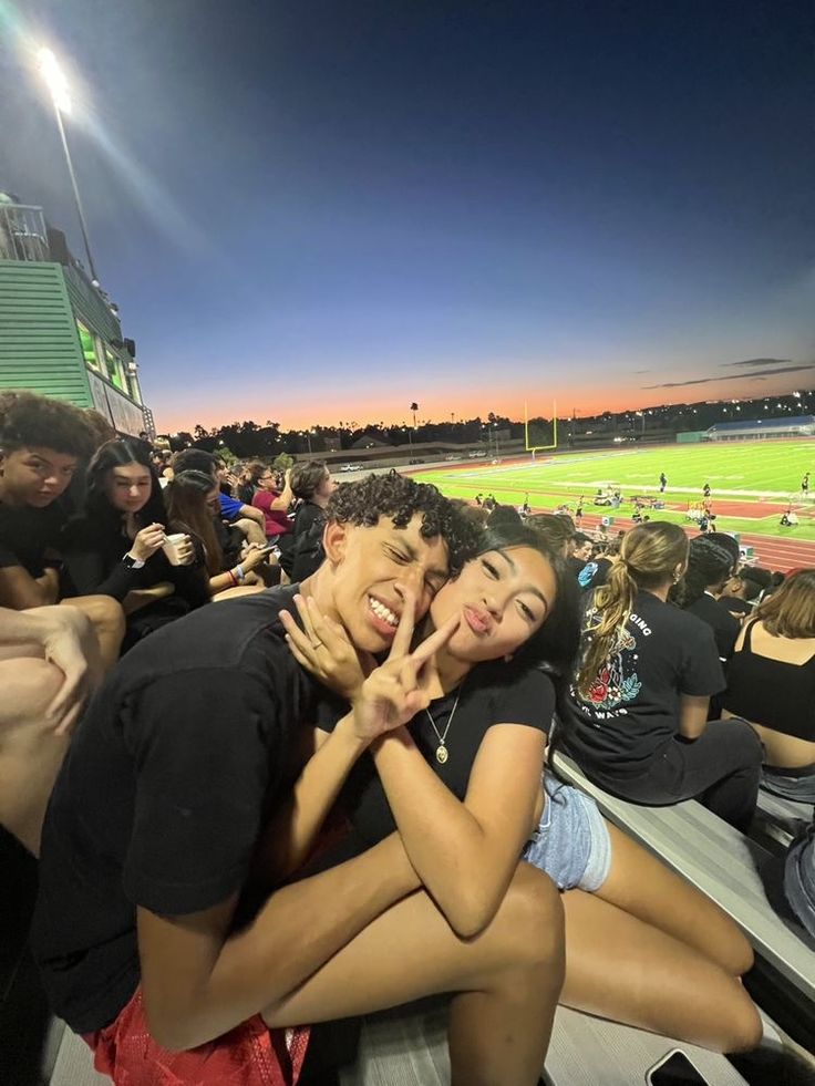 two people are hugging each other in the stands at a baseball game as the sun sets