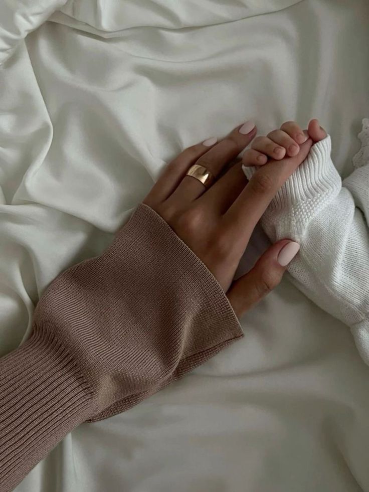 a woman laying in bed with her hands wrapped around the edge of her arm and holding a baby's hand