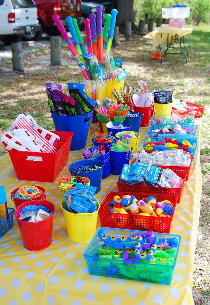 a yellow table topped with lots of plastic buckets filled with toys and candy bars