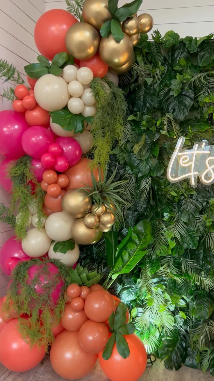 an arrangement of balloons and greenery on the wall