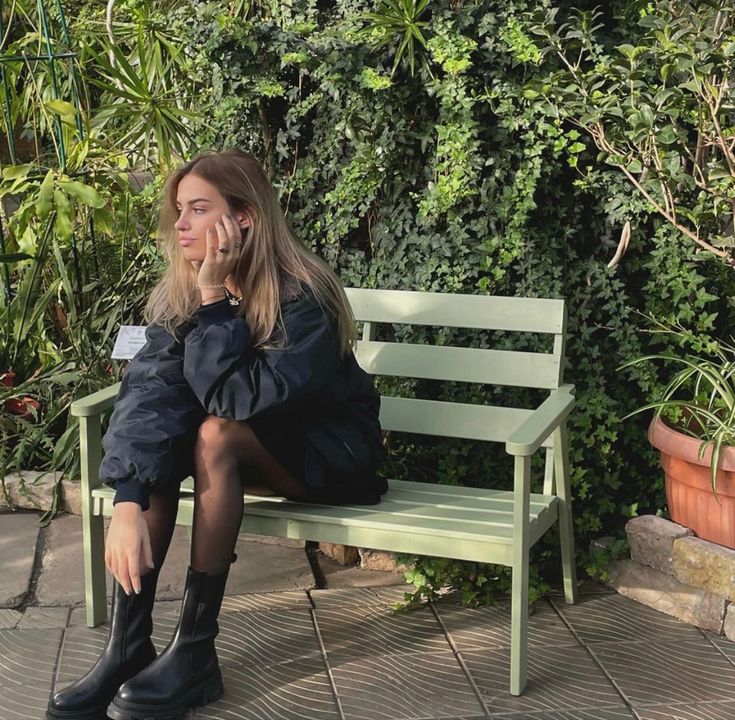 a woman is sitting on a bench talking on her cell phone while wearing black boots