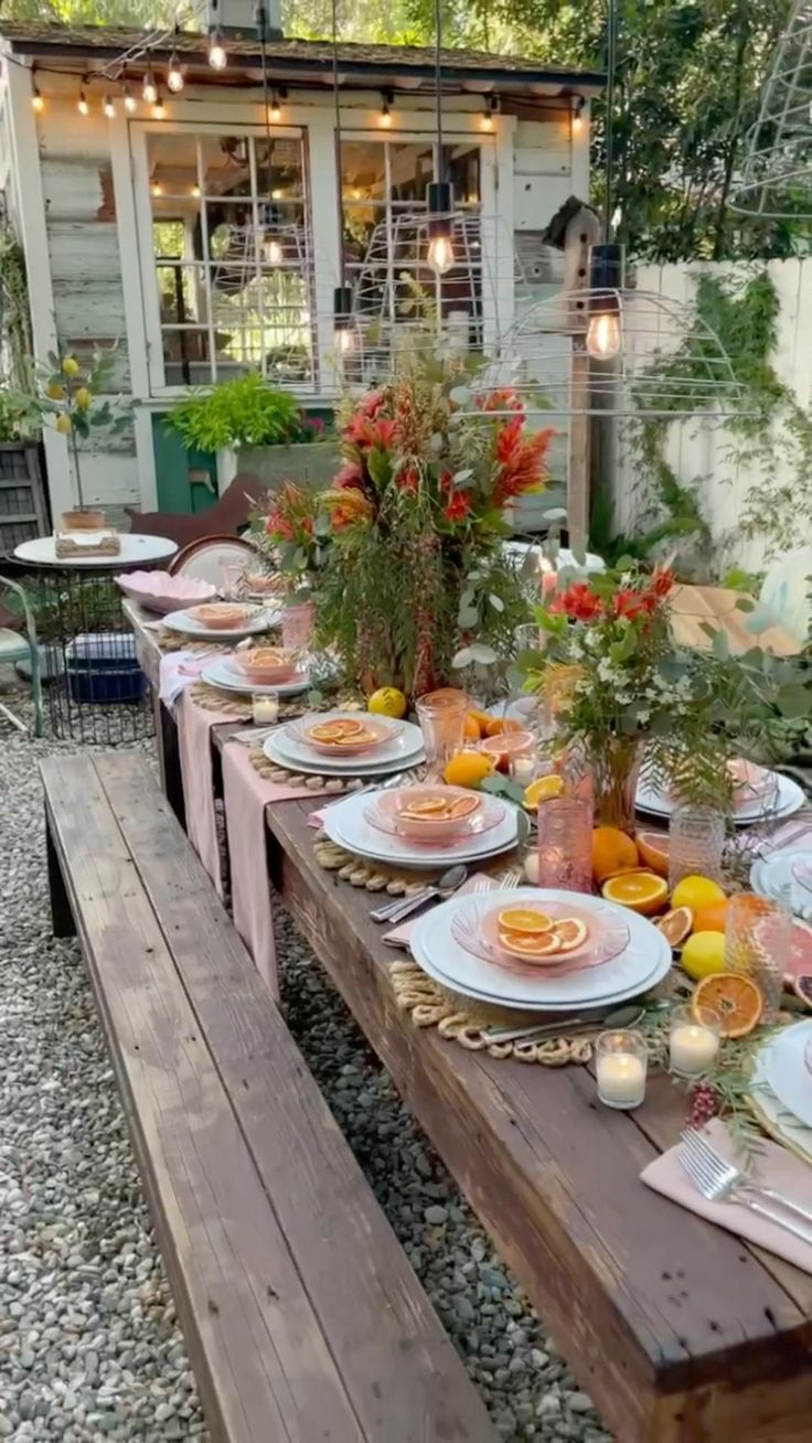 an outdoor table set with plates and utensils on it, next to a wooden bench