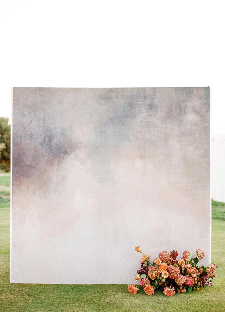 flowers are placed on the grass in front of a large white board with an abstract painting behind it