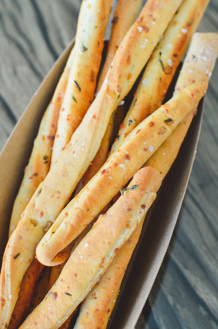 some bread sticks are in a box on a wooden table and it looks like they have been cooked