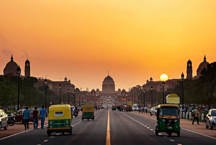 cars and trucks driving down the road in front of an old city building at sunset