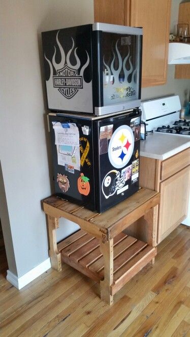 two refrigerators stacked on top of each other in a kitchen with wood flooring