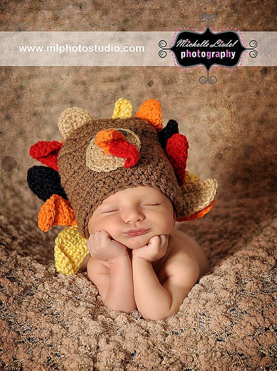 a newborn baby is wearing a crocheted turkey hat and sleeping on his side